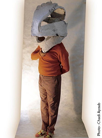 Œuvre photographique représentant un homme debout, poirtant un masque assez gros en forme de sculpture en pierre et d'une forme abstraite.